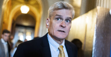 White man in suit and tie with white hair in hallway