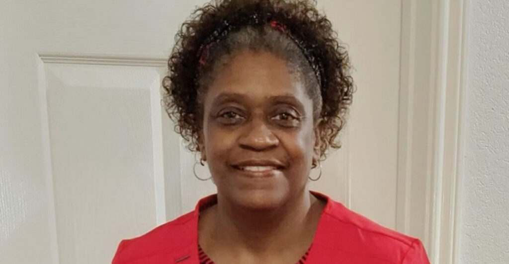 Black woman in a red outfit smiles in front of a white door