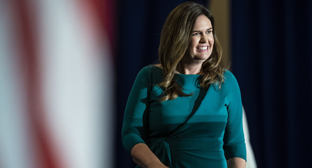 Sarah Huckabee Sanders smiles in a gray dress