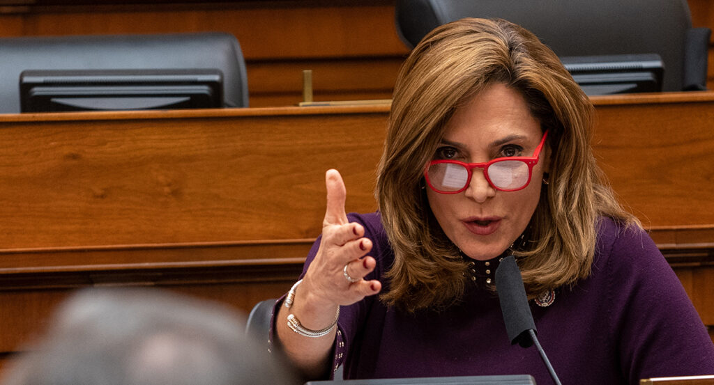 Rep. Maria Elvira Salazar wearing glasses gestures while speaking at a microphone