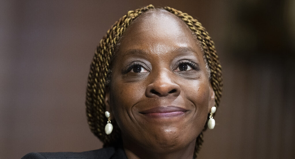 Black lady smiles with white earrings and braided blonde hair