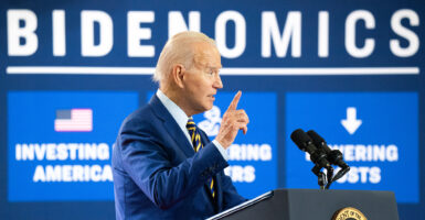 Joe Biden in a blue suit in front of a sign reading "Bidenomics"