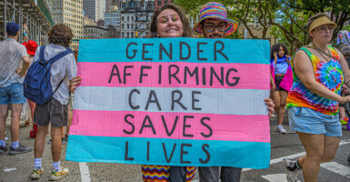 Woman holds transgender flag sign reading "gender-affirming care saves lives"