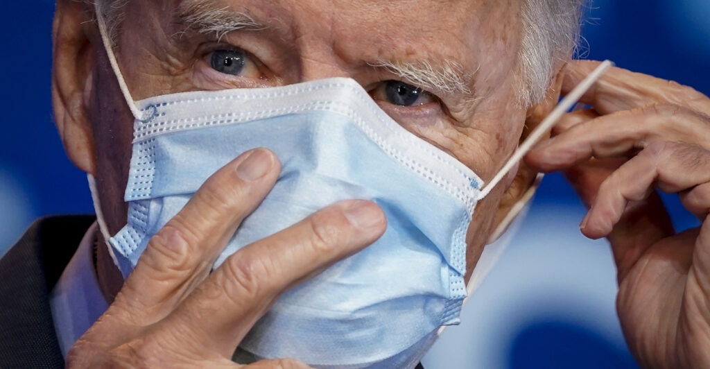 Joe Biden holds a blue mask over his face