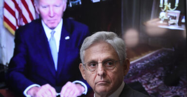 Merrick Garland in a suit with President Joe Biden towering over him