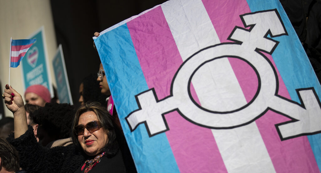 Woman holds transgender flag with transgender symbol