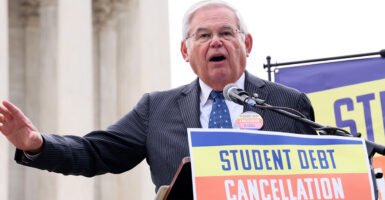 Robert Menendez in a pin-stripe suit speaks in front of a sign reading, "Student Debt Cancellation Is Legal"