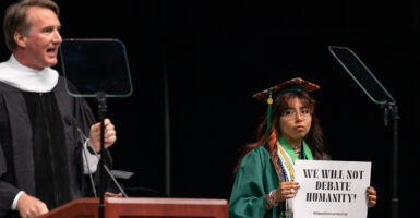 George Mason University graduate holds a sign reading "We will not debate humanity" while Gov. Glenn Youngkin speaks.