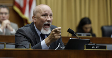Chip Roy gestures in a suit in front of an American flag