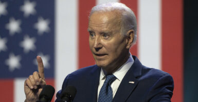 Joe Biden raises his finger in a blue suit with an American flag pin.