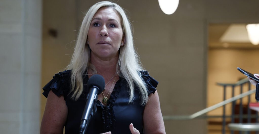 Marjorie Taylor Greene in a dress speaks in front of a microphone