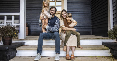 Young family of four sitting on steps in front of house