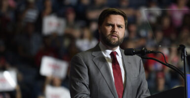 J.D. Vance in a gray suit with a red tie speaks in front of a crowd