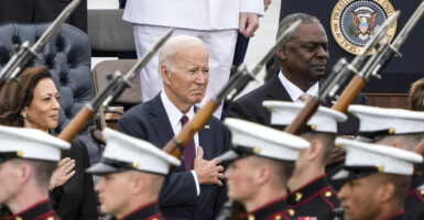 Kamala Harris, Joe Biden, and Lloyd Austin in suits stand in front of soldiers carrying rifles with bayonets.