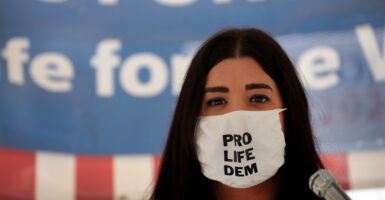 Terrisa Bukovinac stands in front of an American flag while wearing a face mask with the message "pro life Dem"