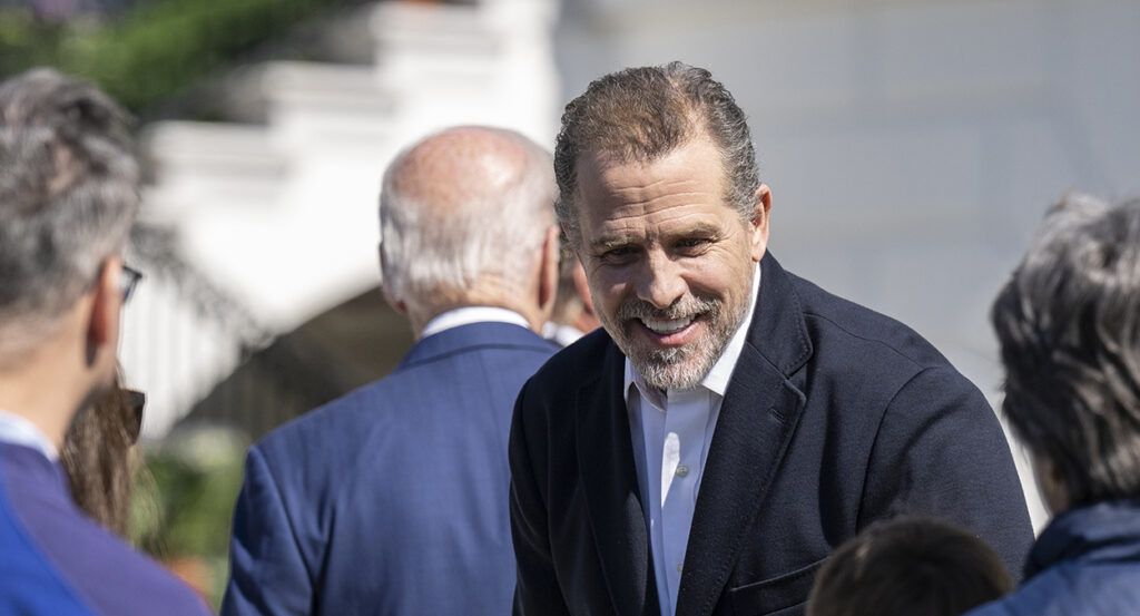 Hunter Biden in a black suit smiles as Joe Biden in a blue suit walks away