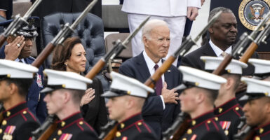 Kamala Harris, Joe Biden, and Lloyd Austin in suits stand behind members of the military in uniform
