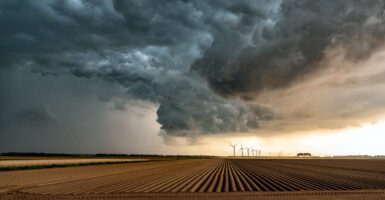 Storm clouds roll over a large farm field.