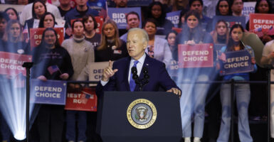 President Joe Biden speaks at a rally at a podium in a suit with a crowd behind him