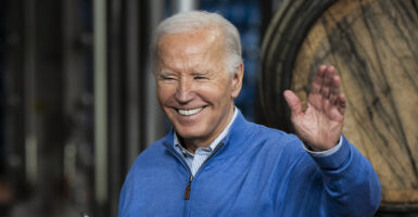 President Joe Biden waves in a blue sweatshirt in front of a beer barrel