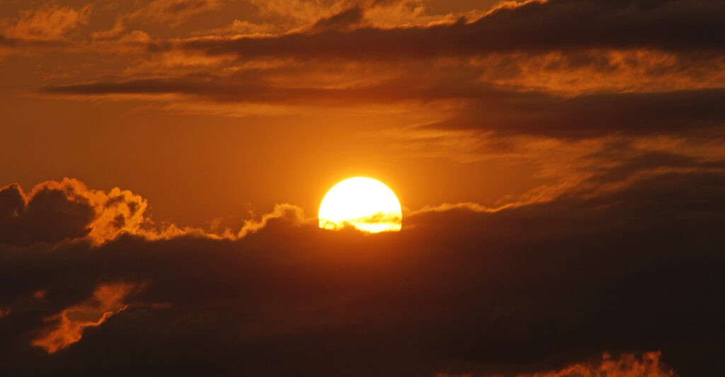 The sun is see rising through the clouds.