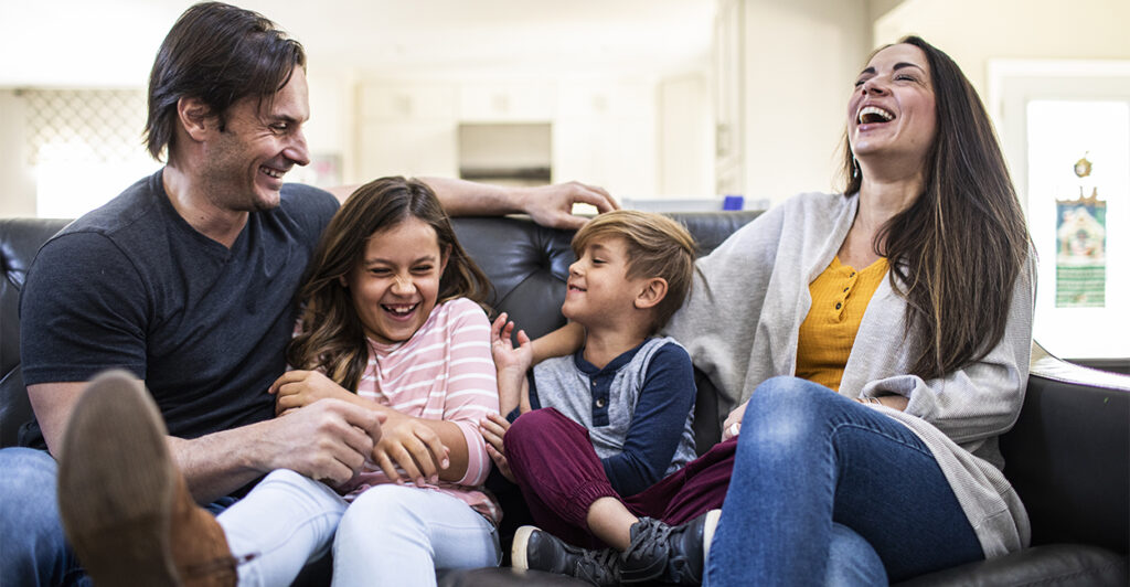 Mom, Dad, and a young son and daughter sitting on a couch at home laughing