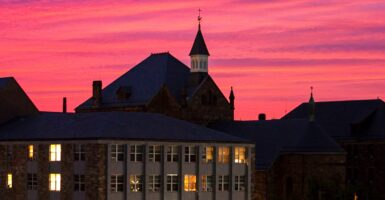 Castle-like building outlines pink sunset with some lights on in windows.