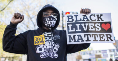 A female protester holds a sign reading "Black Lives Matter" as she also wears a face mask with "Black Lives Matter."