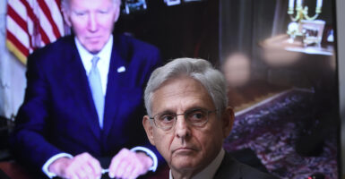 Attorney General Merrick Garland in a suit in front of a screen showing President Joe Biden in a blue suit.