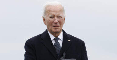 President Joe Biden grimaces with a blank stare in a black suit, holding his hand against his heart.