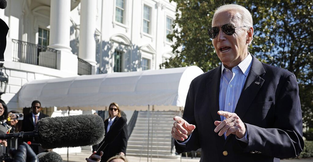 President Biden in a suit jacket with no tie talking to reporters outside the White House