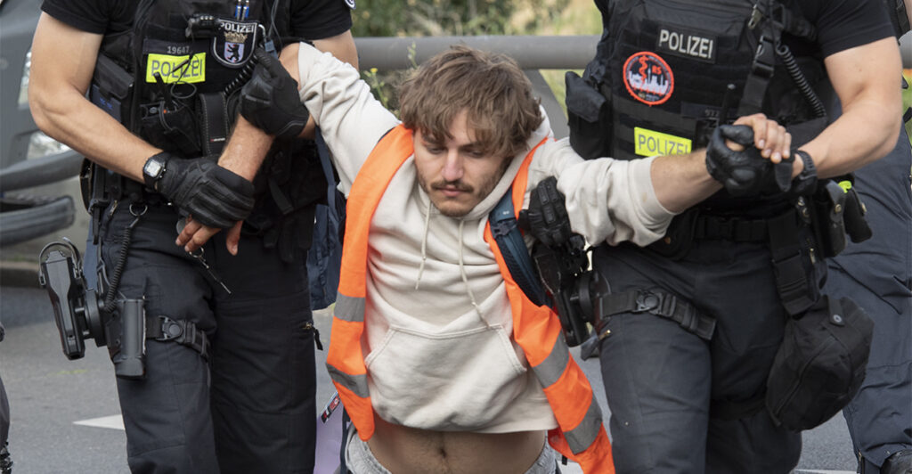Two police officers carry a male demonstrator off the roadway