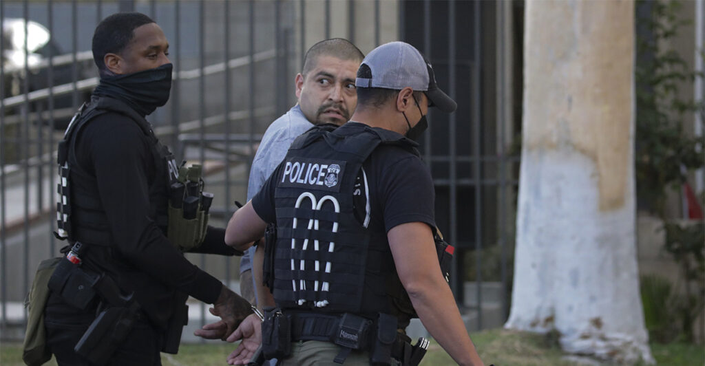 Two police officers walk an illegal immigrant gang member away in handcuffs