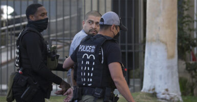 Two police officers walk an illegal immigrant gang member away in handcuffs