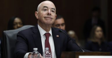 Mayorkas smiles while wearing a black suit and red tie.