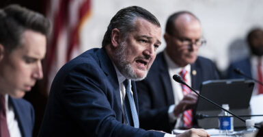 Sen. Ted Cruz, in a blue suit, pounds his fist on the table and speaks out