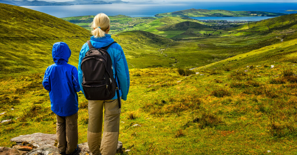 A blonde-haired woman and a young boy, both in blue-green jackets, stare out at the horizon in Ireland.
