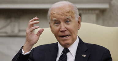 President Joe Biden in a suit with an American flag pin holds his hand near his head