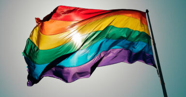 The sun shines behind a rainbow flag meant to symbolize the LGBTQ movement