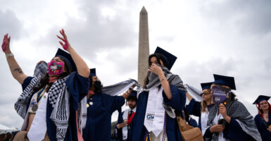 Students wear graduation caps and masks in front of the Washington Monument.