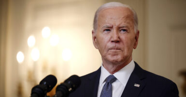 Joe Biden stands in front of a microphone wearing a suit and blue tie.