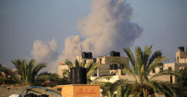 Smoke billows overhead the tops of buildings and palm trees.