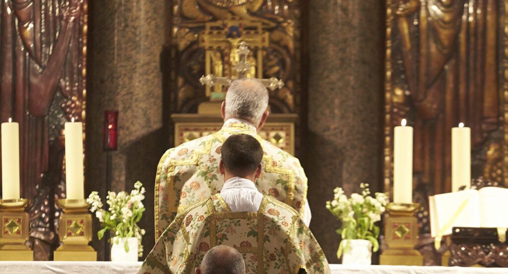 Priests in ornate vestments face the crucifix in a Latin Mass.