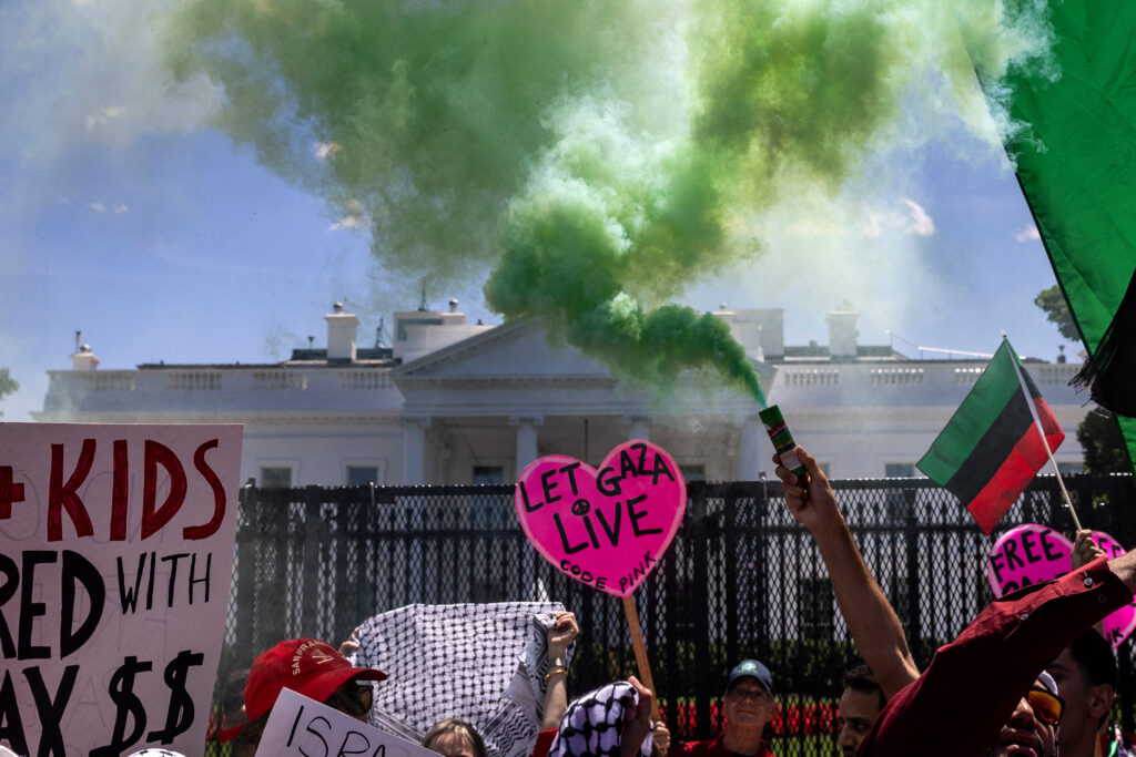 Protesters spraying green smoke and holding signs in front of the White House lawn.