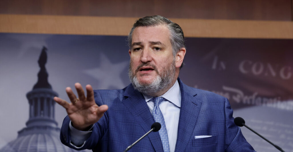 Ted Cruz speaks at a podium into a microphone with an outstretched hand.