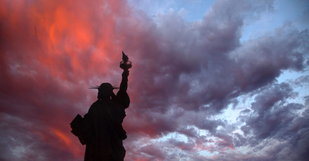 A silhouette of the Statue of Liberty with a sunset background.