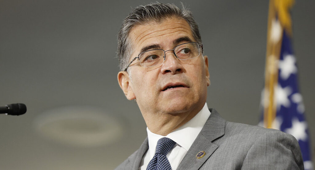 Xavier Becerra in a grey suit looks to the right