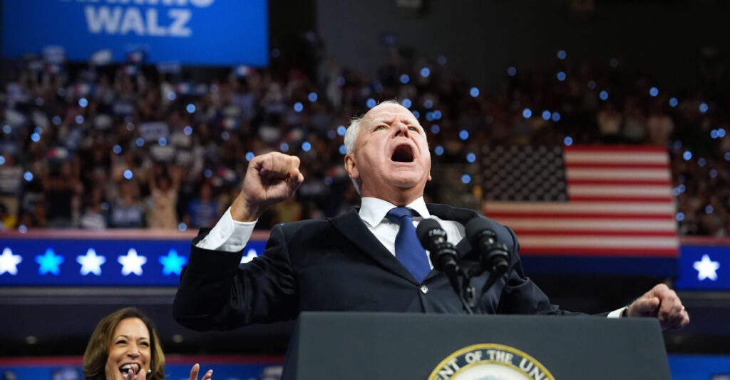 Walz pumps his fist and shouts as he stands at a podium.