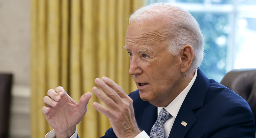 Joe Biden in a blue suit gestures in the White House