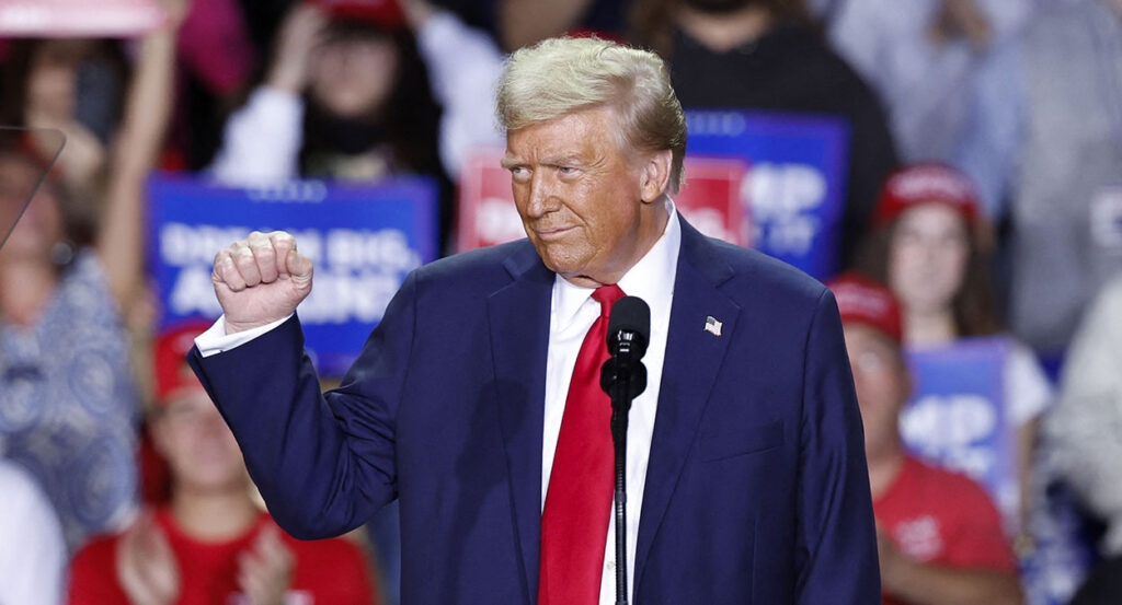 Donald Trump smiles and raises his fist in a blue suit with a red tie